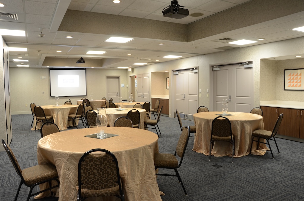 Spacious meeting room at Holiday Inn Express & Suites Mt. Juliet, TN, set with round tables, chairs, and a projector screen for corporate events or receptions.