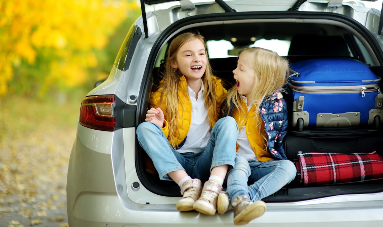 Two young girls sitting in a car packed for a family road trip during the holidays, symbolizing easy holiday travel with kids near Nashville.