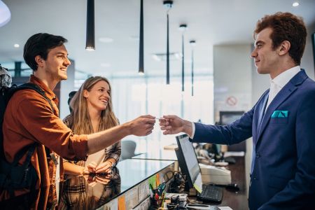 Man and woman checking into hotel and passing credit card to male receptionist.